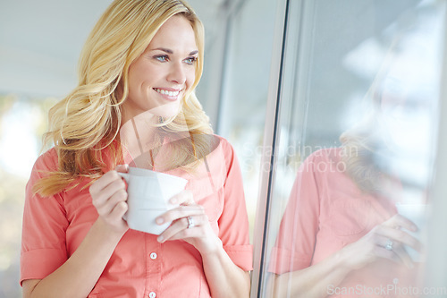 Image of Starting her day with a fresh cup. a beautiful young woman drinking coffee while looking out of her window at home.