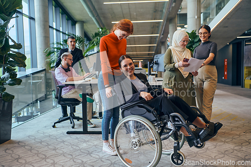 Image of A diverse group of business colleagues is having fun with their wheelchair-using colleague, demonstrating their attention and inclusivity in the workplace