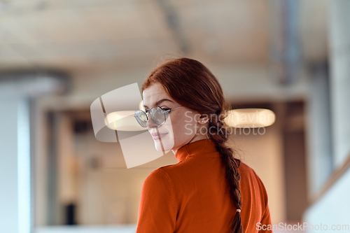 Image of In a vibrant modern startup office, a businesswoman with striking orange hair is immersed in her work at her desk, embodying the dynamic and creative spirit of contemporary entrepreneurship.