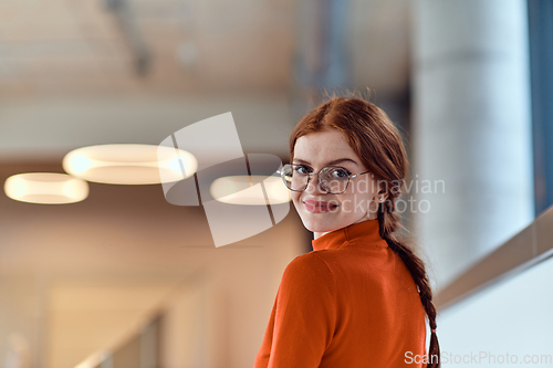 Image of In a vibrant modern startup office, a businesswoman with striking orange hair is immersed in her work at her desk, embodying the dynamic and creative spirit of contemporary entrepreneurship.