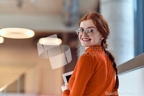 Image of In a vibrant modern startup office, a businesswoman with striking orange hair is immersed in her work at her desk, embodying the dynamic and creative spirit of contemporary entrepreneurship.