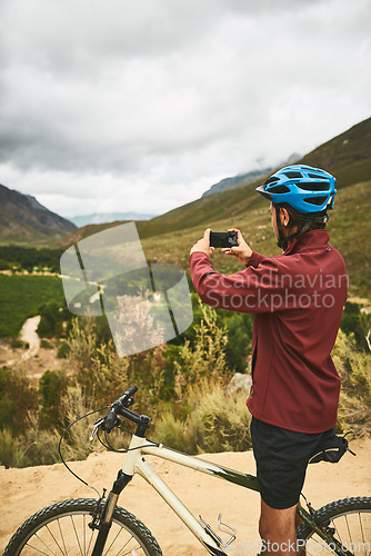 Image of Its a great ride made even better by breathtaking views. a young man taking a photo while cycling along a trail.