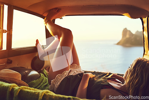Image of Soothed by the sounds of the sea. a young woman relaxing in the back of her car on a roadtrip.