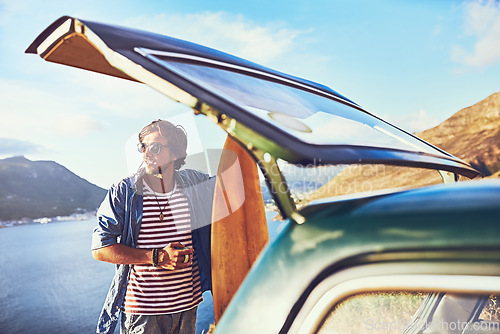 Image of Where will the road lead me next. a happy young man standing outside his car during a roadtrip.