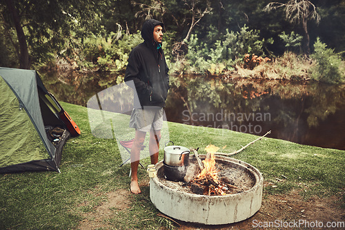 Image of Theres so much to appreciate in the great outdoors. a young man looking thoughtful while preparing food at a campsite fire.