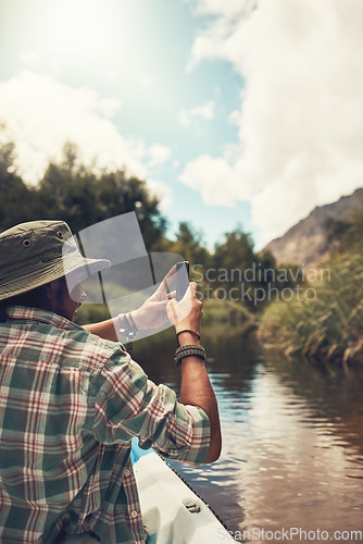 Image of Soaking up the scenic views. Rearview shot of a young man taking photos on his cellphone while enjoying a canoe ride on the lake.