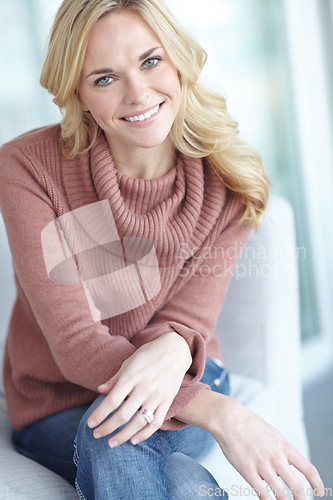 Image of Portrait of a young blonde woman relaxing at home on the sofa in the lounge. Cheerful female sitting on the couch in the living room alone on the weekend. Comfy, smiling and resting inside