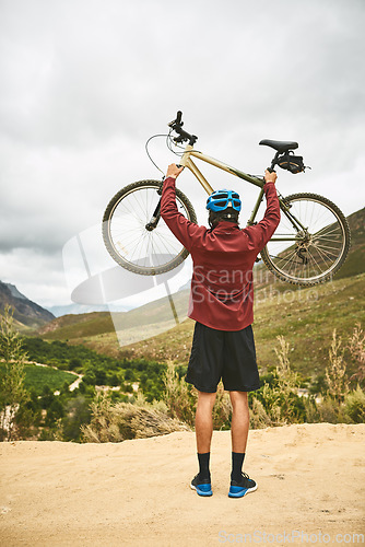 Image of The best adventures are enjoyed on a bike. Rearview shot of a young man standing with his bike raised in victory outside.