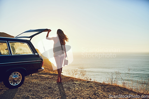 Image of Happiness is a journey, not a destination. Rearview shot of a young woman standing next to her car during a roadtrip.