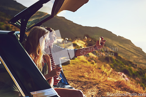 Image of Roadtripping. a happy young couple posing for a selfie with their car on a roadtrip.