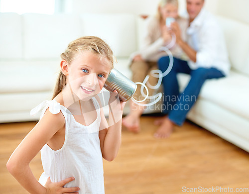 Image of She loves compliments. A little girl listening through a tin can connected to her parents in the background.