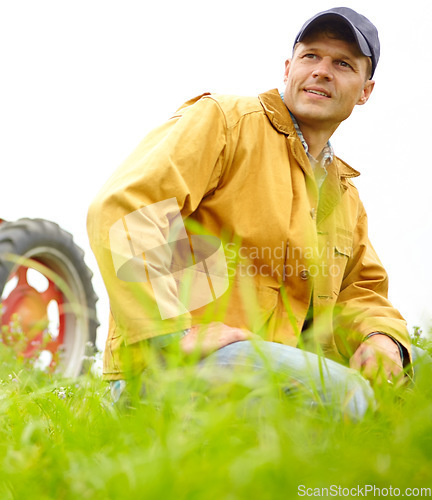 Image of He is at home on the farm. A farmer kneeling in a field with his tractor parked behind him.