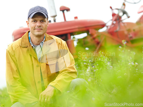 Image of Enjoying the feeling of spring. Portrait of a farmer kneeling in a field with his tractor parked behind him.