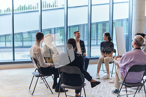 Image of A diverse group of young business entrepreneurs gathered in a circle for a meeting, discussing corporate challenges and innovative solutions within the modern confines of a large corporation