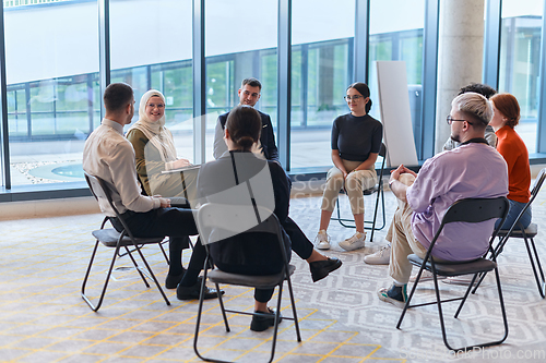 Image of A diverse group of young business entrepreneurs gathered in a circle for a meeting, discussing corporate challenges and innovative solutions within the modern confines of a large corporation