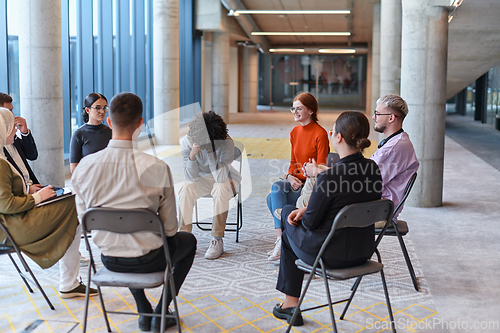 Image of A diverse group of young business entrepreneurs gathered in a circle for a meeting, discussing corporate challenges and innovative solutions within the modern confines of a large corporation