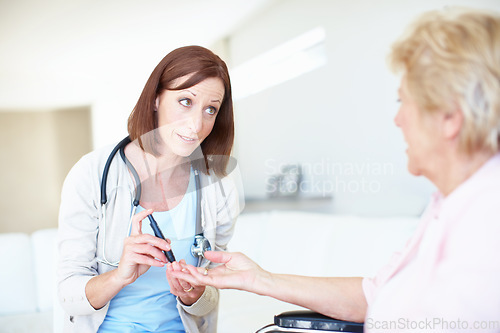 Image of Well get to the bottom of your faintness - DiabetesSenior Care. Mature nurse checking an elderly patients blood sugar levels with a prick to the finger.