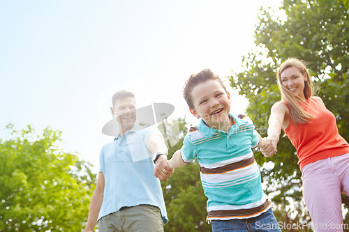 Image of Pulling mom and dad along. Low angle portrait of a happy boy walking hand in hand with his parents.