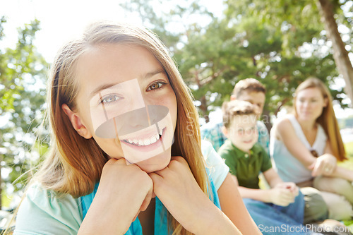 Image of Feeling secure in her familys love. A pretty young girl sitting outdoors in the park with her family in the background.