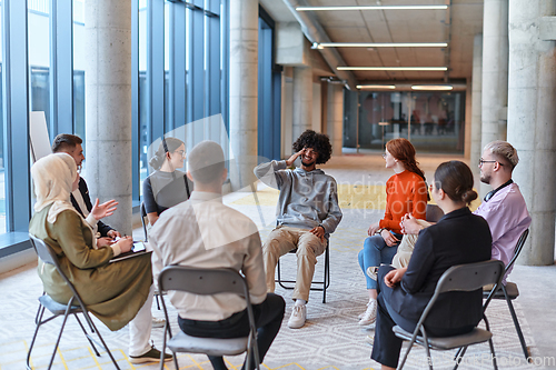 Image of A diverse group of young business entrepreneurs gathered in a circle for a meeting, discussing corporate challenges and innovative solutions within the modern confines of a large corporation