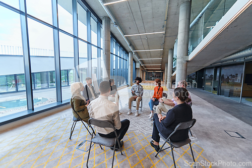 Image of A diverse group of young business entrepreneurs gathered in a circle for a meeting, discussing corporate challenges and innovative solutions within the modern confines of a large corporation