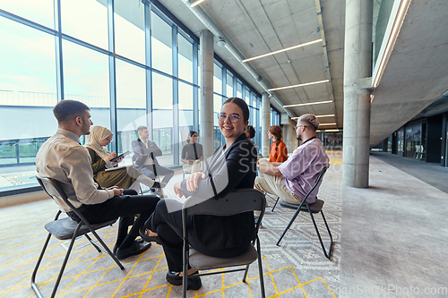 Image of A diverse group of young business entrepreneurs gathered in a circle for a meeting, discussing corporate challenges and innovative solutions within the modern confines of a large corporation