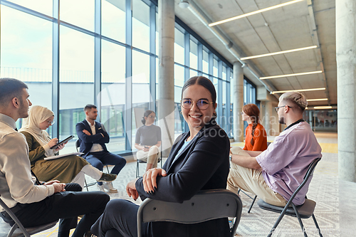 Image of A diverse group of young business entrepreneurs gathered in a circle for a meeting, discussing corporate challenges and innovative solutions within the modern confines of a large corporation