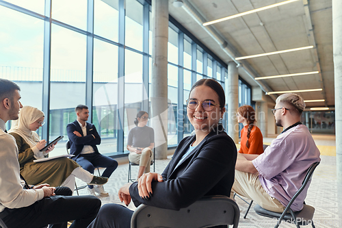 Image of A diverse group of young business entrepreneurs gathered in a circle for a meeting, discussing corporate challenges and innovative solutions within the modern confines of a large corporation