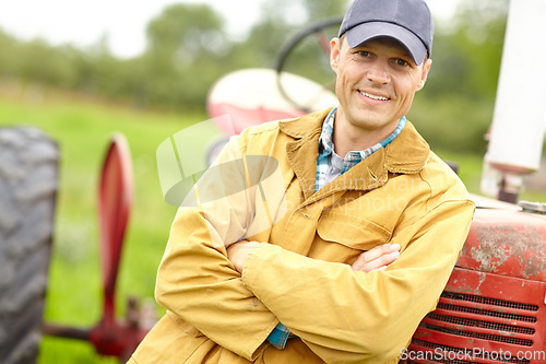 Image of Another good days work. Portrait of a smiling farmer with his arms crossed standing infront of his tractor.