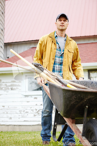 Image of I work hard. A serious man standing outside with his wheelbarrow.