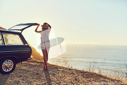 Image of This is where she comes to unwind. Rearview shot of a young woman standing next to her car during a roadtrip.