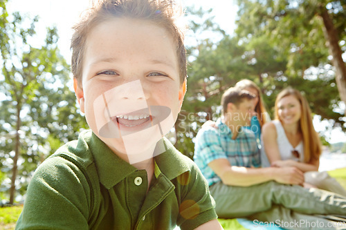 Image of Enjoying family time in the park. A happy little boy sitting outdoors with his family on a sunny day.