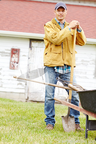 Image of Almost time to start digging. Portrait of a happy man standing next to a wheelbarrow with a spade in his hand.