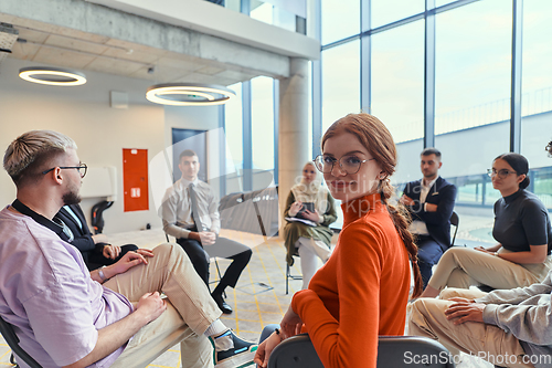 Image of A diverse group of young business entrepreneurs gathered in a circle for a meeting, discussing corporate challenges and innovative solutions within the modern confines of a large corporation