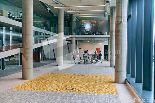 Image of A diverse group of young business entrepreneurs gathered in a circle for a meeting, discussing corporate challenges and innovative solutions within the modern confines of a large corporation