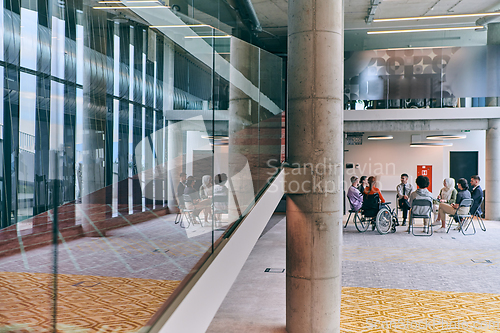 Image of A diverse group of young business entrepreneurs gathered in a circle for a meeting, discussing corporate challenges and innovative solutions within the modern confines of a large corporation