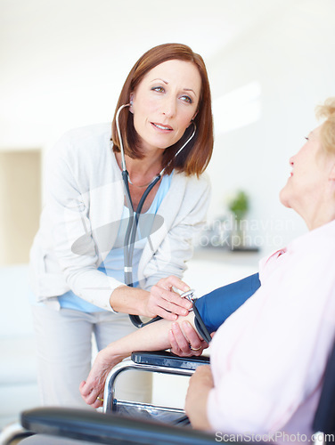 Image of Checking her pulse and blood pressure - Senior Care. Mature nurse checks an elderly female patients blood pressure.