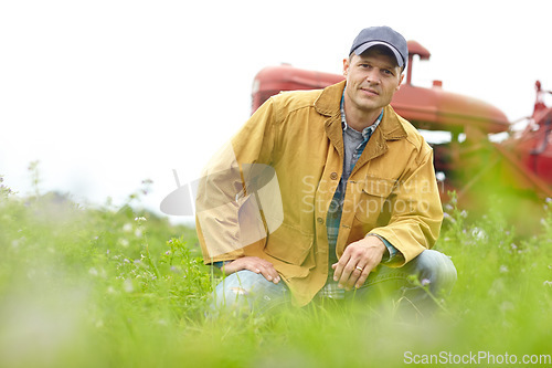 Image of Being a farmer is part of who I am. Portrait of a farmer kneeling in a field with his tractor parked behind him.