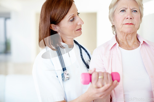 Image of Strength and rehabilitation - Senior Health. Determined elderly female is assisted by her nurse as she lifts a dumbbell.