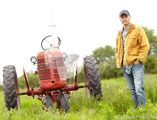 Image of My tractor and I are in this together. Full length portrait of a farmer standing next to his tractor in a field.