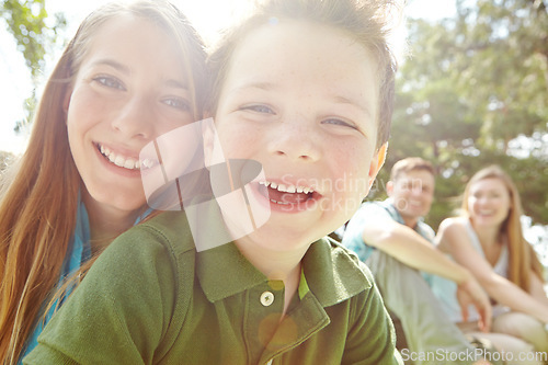 Image of Shes a caring big sister. A happy little boy sitting outdoors with his family on a sunny day.