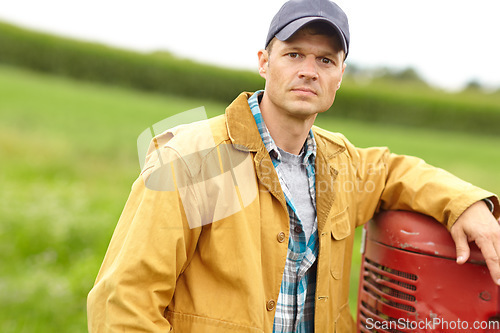 Image of Serious about farming. Portrait of a serious farmer with his arm resting on the hood of his tractor while he stands in an open field.
