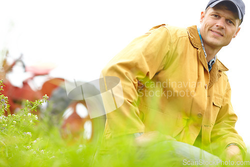 Image of Confident in tthe results of this years harvest. Portrait of a farmer kneeling in a field with his tractor parked behind him.