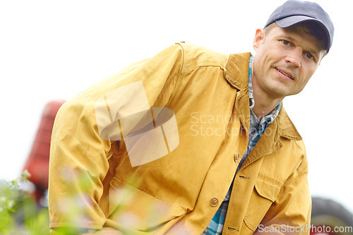 Image of The lifestyle of a true farmer. Portrait of a farmer kneeling in a field with his tractor parked behind him.