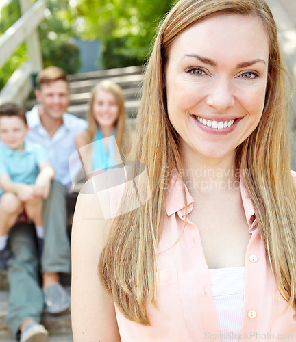 Image of Im one proud mom. Smiling attractive mother with family sitting behind her while outdoors.