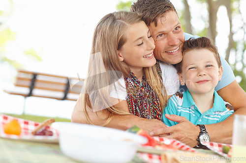 Image of Picnic lunch with dad. Father hugging his daughter and son at the picnic table.