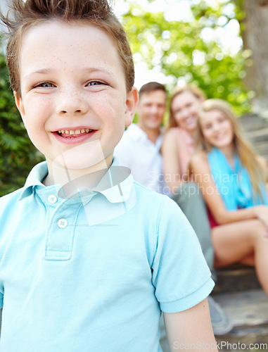 Image of This is my family. Cute little boy with family sitting behind him while outdoors.