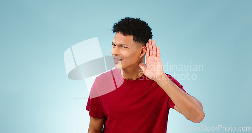 Image of Portrait, overhearing and hand gesture for eavesdropping with a man listening in studio on a blue background. Emoji, communication and secret with a confused young person in doubt about news