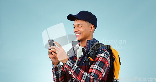 Image of Hiking, smile and typing with man, cellphone and adventure with social media on blue studio background. Person, hiker and model with a smartphone, mobile user and contact with journey or mockup space