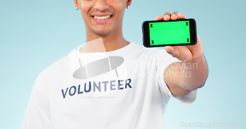 Image of Hand, phone and green screen with a volunteer man in studio on blue background for marketing or charity. Smile, space or advertising and a person showing chromakey on a display with tracking markers